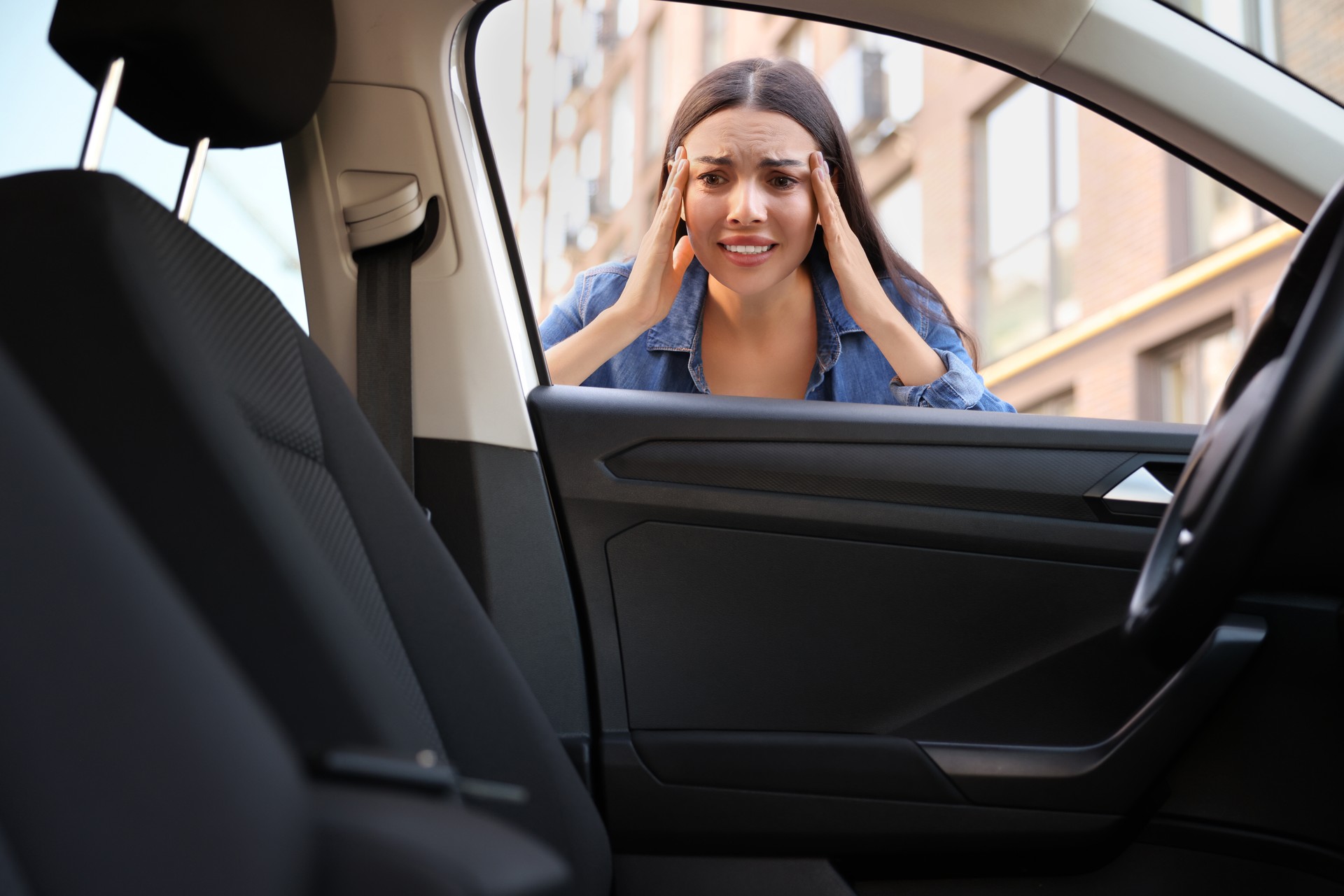 Automobile lockout, key forgotten inside. Emotional woman looking through car window